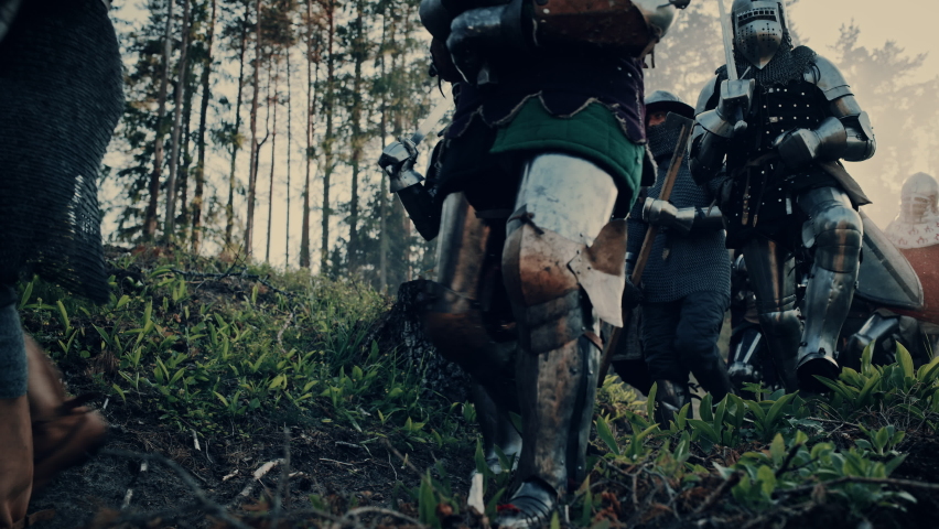 Epic Invading Army of Medieval Soldiers Marching Through Forest. Armored Warriors with Swords Moving to Battlefield. War, Battle, Crusades in Dark Ages. Cinematic Historical Reenactment. Low Angle Royalty-Free Stock Footage #1077268091