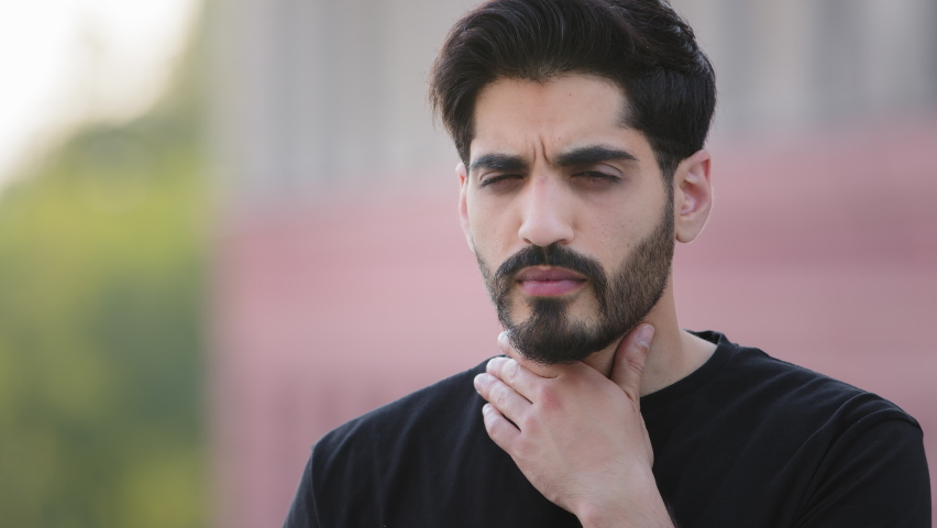 Heads hot bearded Indian young man touching neck, suffering from strong throat sore, angina. Unhealthy unhappy guy feeling pain while swallow, voice loss, suffocation, spasm. Doctor's help required | Shutterstock HD Video #1077268121
