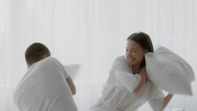 Cheerful young couple pillow fighting in bedroom, happy millennial man and woman having fun at home, joyful spouses laughing while playing in bed, enjoying spending time together, slow motion footage - Powered by Shutterstock - Get 15% off with code: PIKWIZARD15