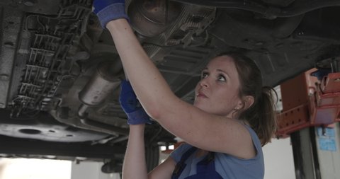 Professional female mechanic working under a car in the auto repair shop