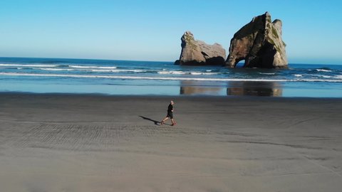 Man running at beautiful New Zealand spot. Sandy Wharariki Beach with iconic archway islands