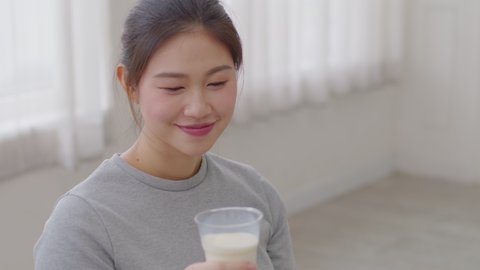 Healthy Young Asian woman Drinking milk with calcium for strong bone at home, Smiling woman holding soy milk on glass enjoy with nutrition wellness life, Wellness with natural milk fresh Concept