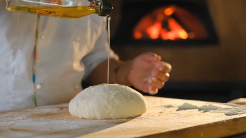 Making pizza dough. The cook kneads the dough and sprinkles it with olive oil. Cooking pizza in a pizzeria. A man pours vegetable oil over the dough.