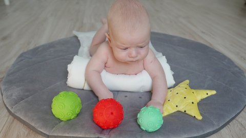 Cute baby lying on his tummy on play mat, 3 month old newborn infant boy playing with colorful sensory balls on the floor. High quality 4k footage
