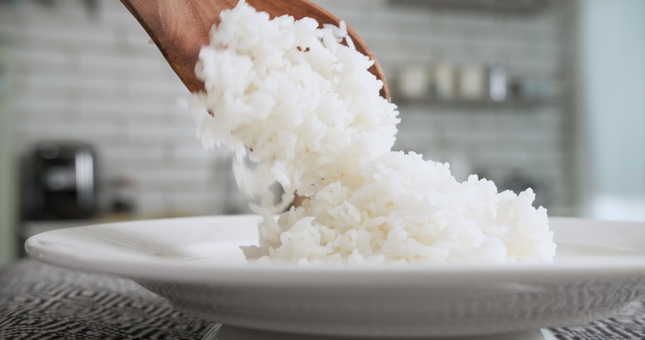 Fluffy steaming freshly cooked jasmine rice placed on white plate using wooden rice ladle  | Shutterstock HD Video #1077287972