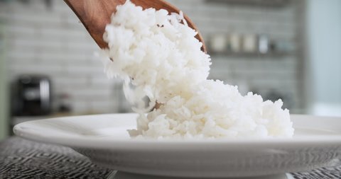 Fluffy steaming freshly cooked jasmine rice placed on white plate using wooden rice ladle 