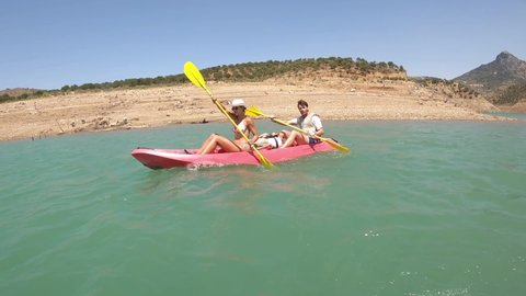 Zahara, Cadiz, Spain, August 3, 2021: Couple kayaking in water reservoir close by bulls, cows, and goats that stand by the shore. 