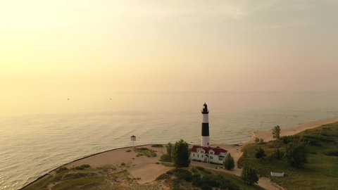 Establishing shot of a lighthouse on the shore of Lake Michigan. Sand dunes, beach at sunset. Ludington State Park, Michigan state, United States of America. Aerial view, from above, fly over