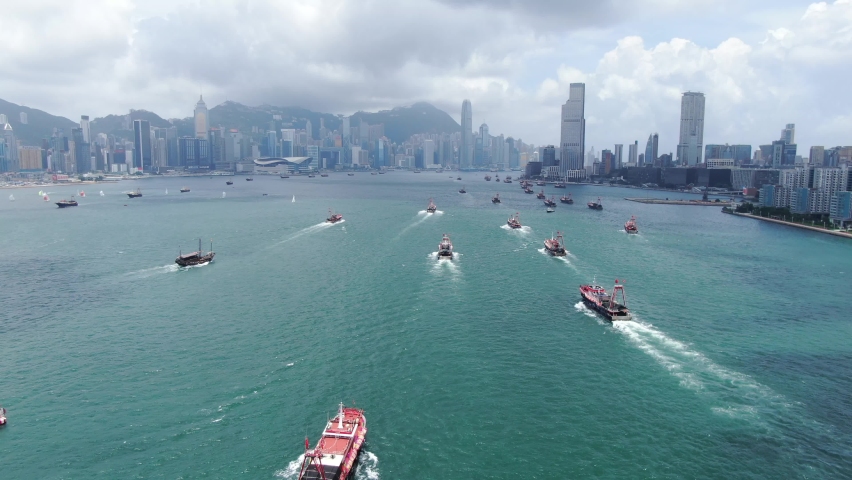 Convoy of local Fishing boats causing in Hong Kong Victoria bay, with city skyline in the horizon, Aerial view.