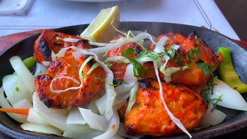 Traditional Indian Tandoori chicken with onions on a very hot plate with steam smoke in a restaurant, 4K static shot