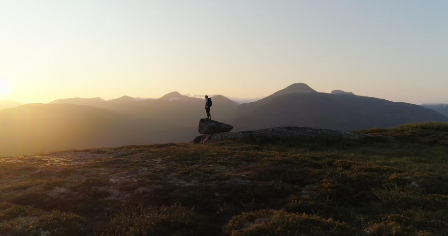 Norwegian climber on rock looking at northern mountains in sunset - aerial orbit