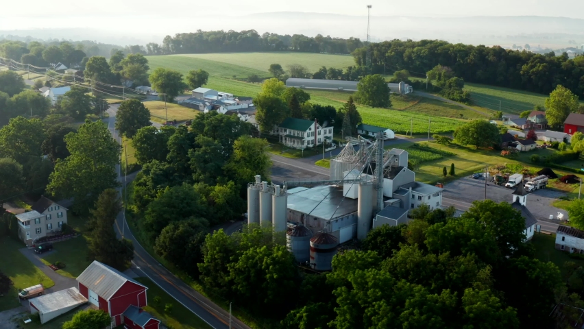 Rural small town in USA. Aerial orbit of feed mill and surrounding farm land in summer morning mist and light.