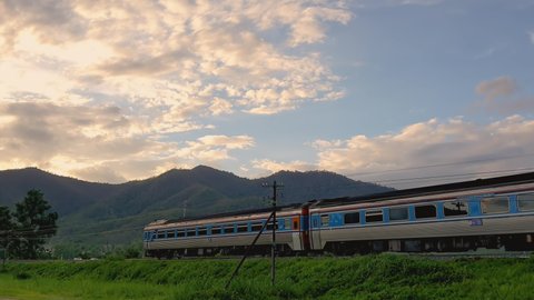 Thailand passenger train run at speed on the railway during beautiful sunset. Handheld pan camera right to left.