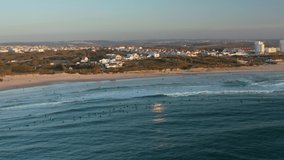 Baleal, Portugal, Europe. Picturesque scenery of an idyllic harbor with coastal town in the background. Aerial view of a seascape with people on surfing boards within waves. High quality 4k footage