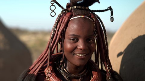Happy young Himba woman smiling, standing next to her hut in a traditional Himba village near Kamanjab in northern Namibia, Africa. 