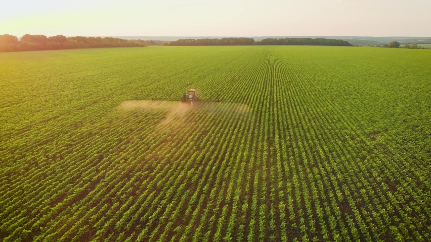 Aerial view of farming tractor spraying on field with sprayer, herbicides and pesticides at sunset. Farm machinery spraying insecticide to the green field, agricultural natural seasonal spring works. Royalty-Free Stock Footage #1077307580