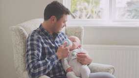Father feeding baby son with bottle sitting in chair at home together - shot in low motion - Powered by Shutterstock - Get 15% off with code: PIKWIZARD15