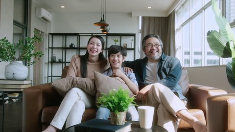 happiness sweet Asian family father mother and son sitting together on sofa watching movie from the tv at home. laugh smiling Asian family at home isolation quarantine moment in lockdown state order.