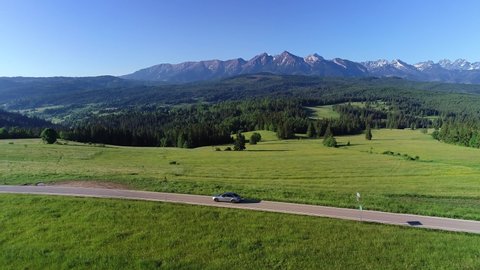 Aerial view of mountain road and luxury sedan driving on an empty road. In the background wide Tatra mountains range. Concept: Vacations in mountains, family road trip, traveling, going to holidays.