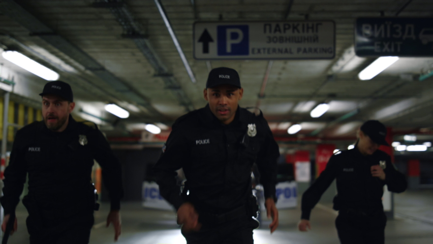 Police officers running after criminal on underground parking. Policewoman and policemen chasing robber. Female and male cops in uniform trying to catch offender  Royalty-Free Stock Footage #1077318425