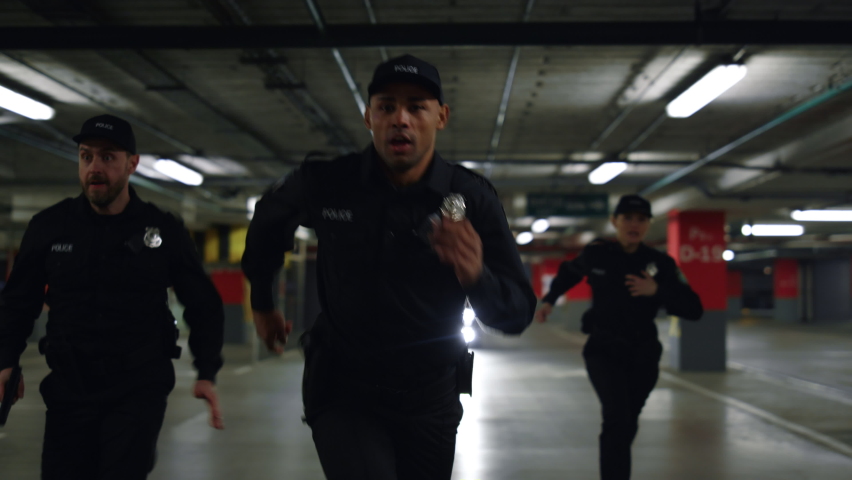 Police officers running after criminal on underground parking. Policewoman and policemen chasing robber. Female and male cops in uniform trying to catch offender  Royalty-Free Stock Footage #1077318425