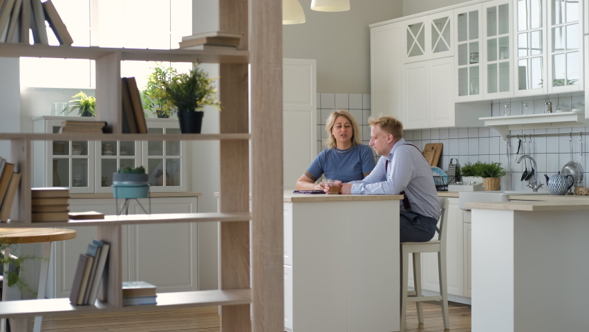 Mature Middle-Aged Mother with her Grown Son Chatting and Drinking Tea while Sitting at Table in the Kitchen. Bonding and Family Reunion, Mothers Day Concept