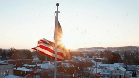 Snow falling at dawn, dusk. Static aerial shot of American Flag on flagpole waving in breeze. Backlit flag with starburst sun effect. Cold winter holiday season with snow on rooftops. - Powered by Shutterstock - Get 15% off with code: PIKWIZARD15