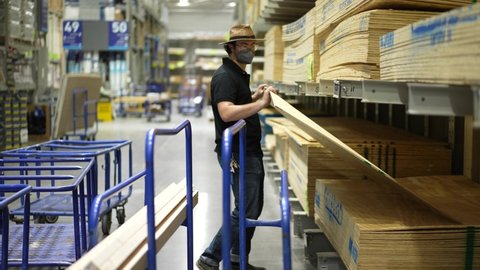 Winchester, VA, USA - 08 04 2021: Home improvement man chooses sheet of plywood and puts it on his shopping cart in big box hardware store.