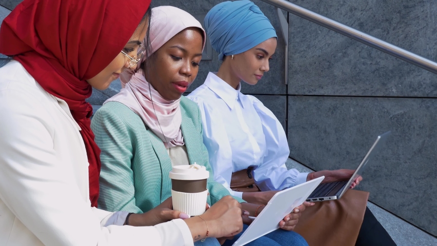 Group of beautiful girls spending time together outdoor. Young women with hijab and modern elegant clothes doing activities in the city center