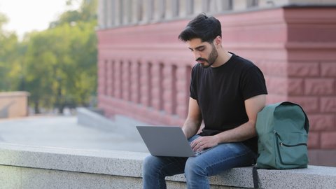 Young Indian bearded man with mustache typing texting on modern laptop keyboard, middle eastern male employee sit outdoors working on computer, consult client or studying online, technology concept