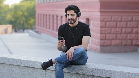 Young bearded indian arabic male hipster in headphones enjoying to music, carefree dark-haired middle eastern student wearing earphones, dancing listening to favorite tracks, new popular hit online