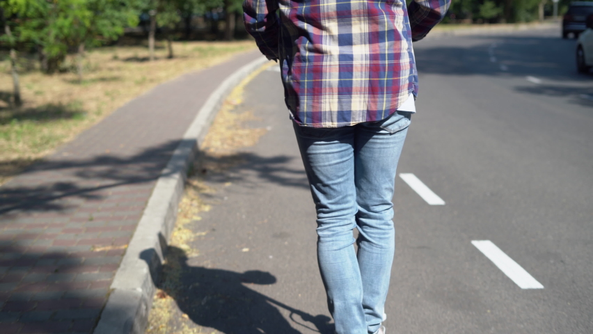 The back view of a man in a shirt rides an electric scooter along a bicycle lane.