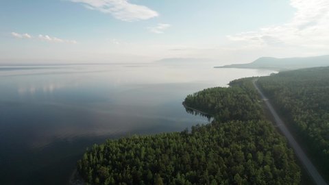 Epic cinematic aerial view Lake Baikal in morning. Turquoise water in a mountain forest lake with pine trees. Aerial view of blue lake and green forests. View on the lake between mountain forest.