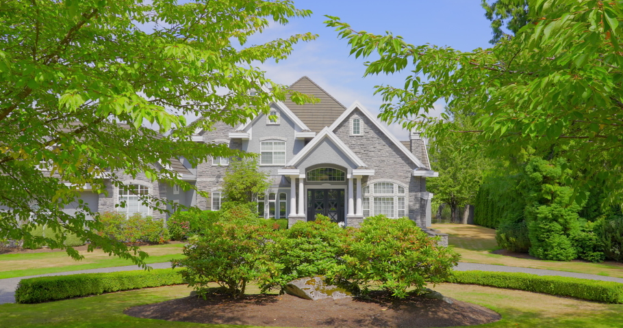 Establishing shot of two story stucco luxury house with garage door, big tree and nice landscape in Vancouver, Canada, North America. Day time on August 2021. ProRes 422 HQ.