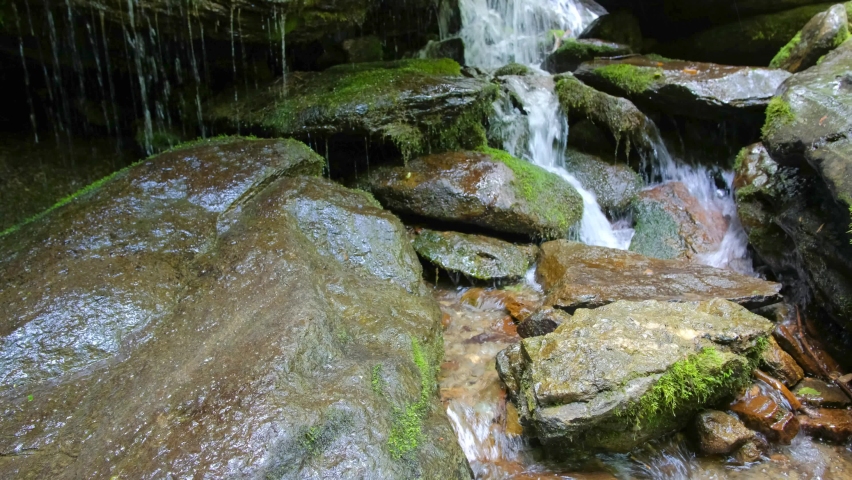Close up shot of water cascading over stones and moss covered rocks.