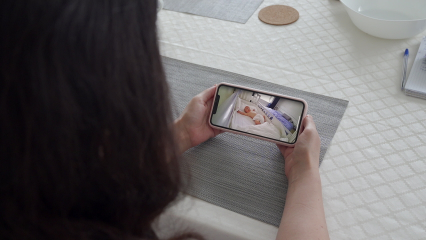 Mother using ip wireless security camera as baby video monitor on mobile phone, woman watching her sleeping baby in real-time. High quality 4k footage | Shutterstock HD Video #1077345041