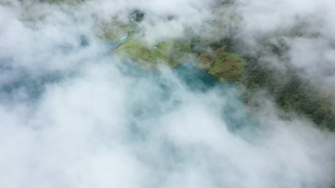 A cloud passing over the reservoir of the Roselend dam and the surrounding meadows in Savoie, Auvergne-Rhône-Alpes, France, in the fall, in a drone during a day under the clouds.