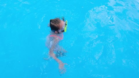 Girl somersaults and plays in the transparent blue swimming pool water. Child have fun in swim pool. Full HD slow motion video.