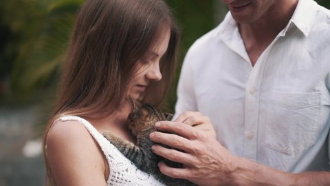 Close up slowmotion video of couple play with small little kitten. Beautiful woman and strong man hold tabby cat on woman's chest. Animal lovers concept. High quality FullHD footage.