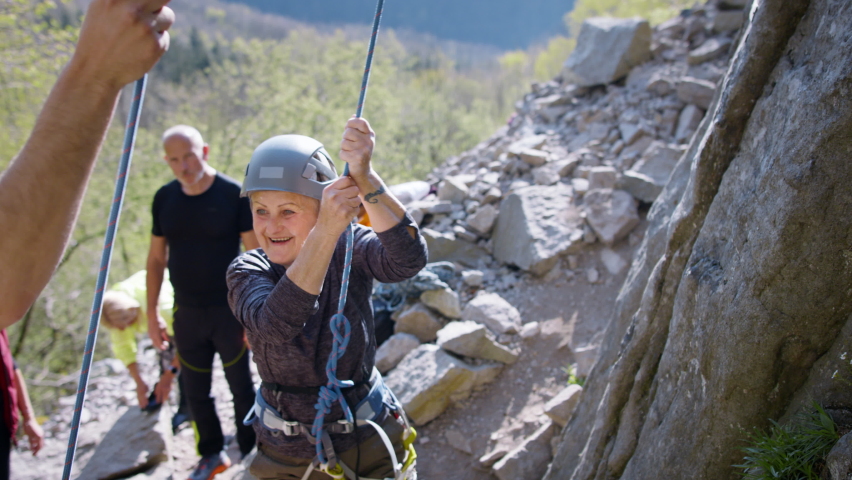 Group of seniors with instructor celebrating successful rocks climbing outdoors in nature, active lifestyle.
