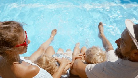 Top view of beautiful family sitting on the edge of the pool and having fun together.