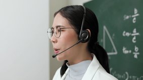 Young asian teacher woman teaching holding chalk wearing headset video conference with student looking camera. Female teacher training the mathematics in classroom blackboard online course.
