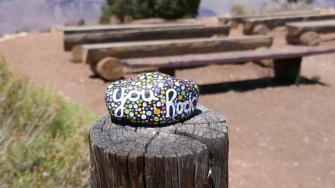 Kindness rock with painted you rock message on wooden post with outdoor classroom out of focus in background