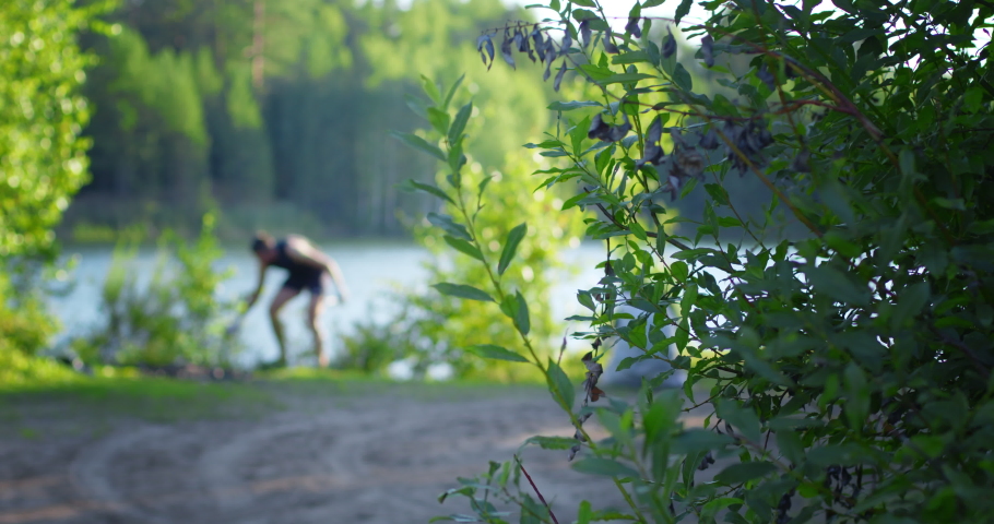 Man collects trash on the lake. Focus on the green leaves on the foreground