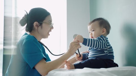 Asian female Pediatrician doctor examining little cute Baby boy with stethoscope in medical room at hospital.