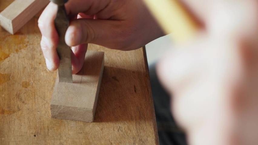carpenter cuts a square hole on the board with a chisel. wood carving in a carpentry workshop. the art of woodworking. the sound of hand carpentry tools