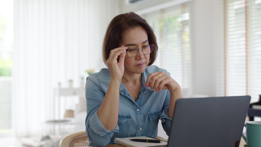 Asia adult upset sad people or pensive SME owner latin lady sit at home brownout work on desk laptop tired bored pain in mental health care issue, job loss life crisis or think hard of debt loan. | Shutterstock HD Video #1077361859