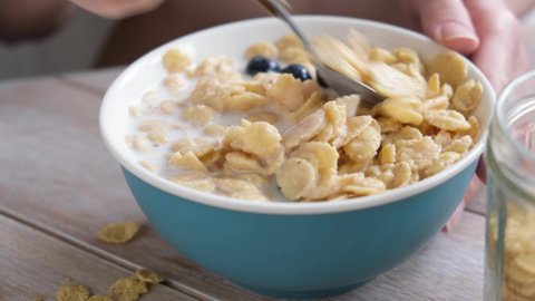 Cornflakes with milk and blueberries in bowl. Unrecognizable young woman eating sugar free corn flakes with almond milk for breakfast