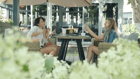 Carefree women are dancing in outdoor cafe while female friend is recording video and laughing having fun together. Technology and friendship concept.