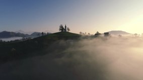 Aerial landscape of mountain hills covered in fog and Saint Thomas church, Slovenia on sunset